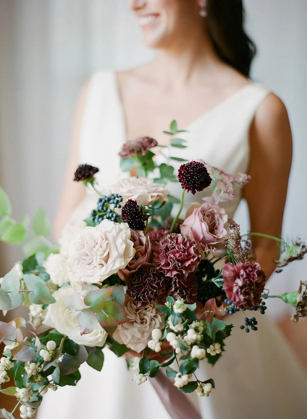 Romantic bouquet with red and pink roses, green foliage, and white ribbon on wooden table.