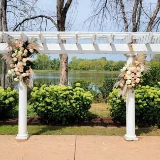 Outdoor wedding arch decorated with pink and white flowers near a lake