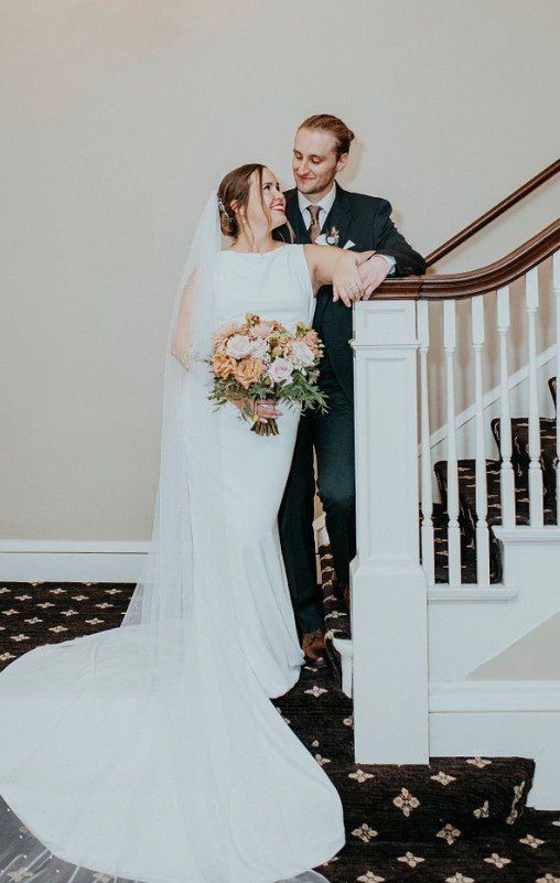Bride and groom sharing a tender moment on staircase during wedding, with the bride holding a bouquet of flowers.