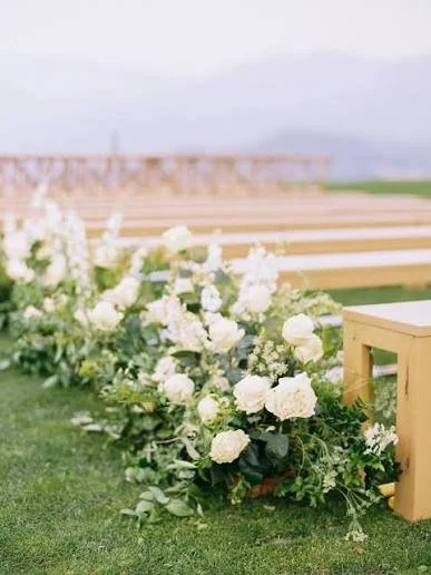 White floral arrangement on a grassy area with wooden benches in the background.
