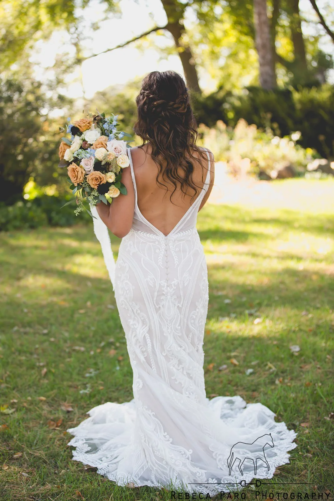 A bride in a white wedding dress holding a bouquet of flowers standing outdoors in a wooded area.