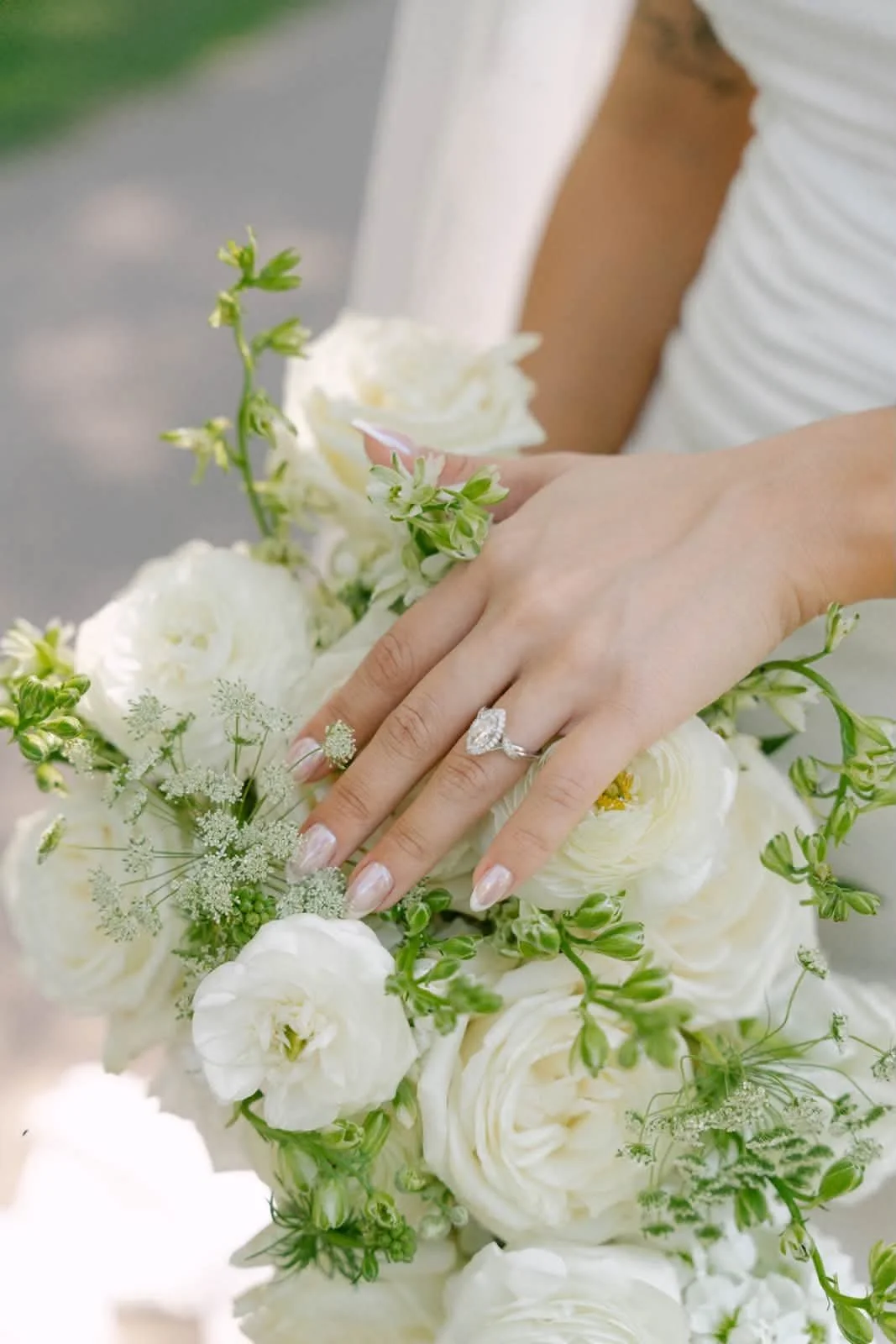Close-up of a woman's hand with a diamond engagement ring resting on a floral bouquet of white and green flowers.