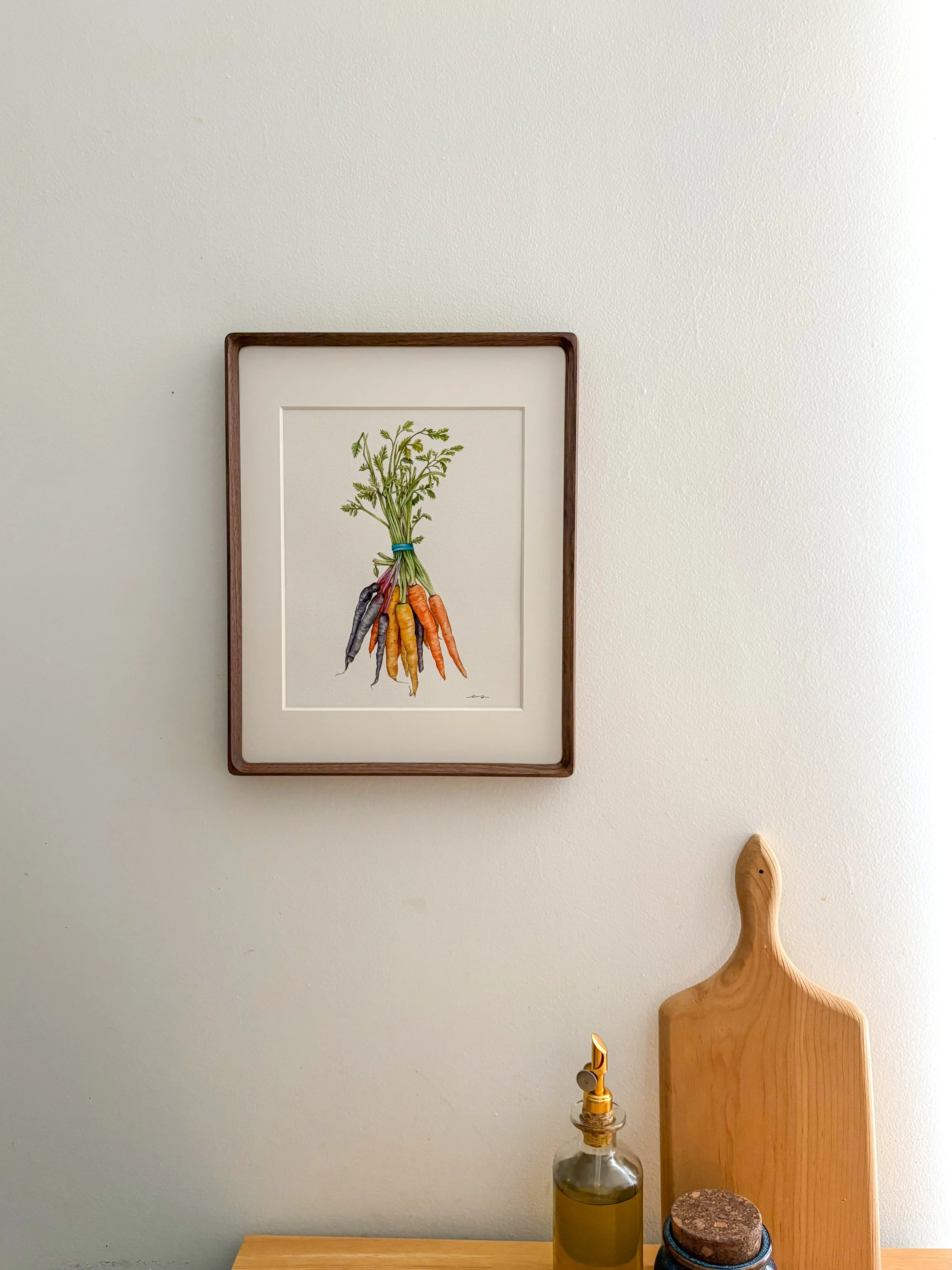 Original framed watercolor painting of a bundle of rainbow carrots in purple, yellow and orange tied with a blue rubber band and green tops, in a dark walnut frame