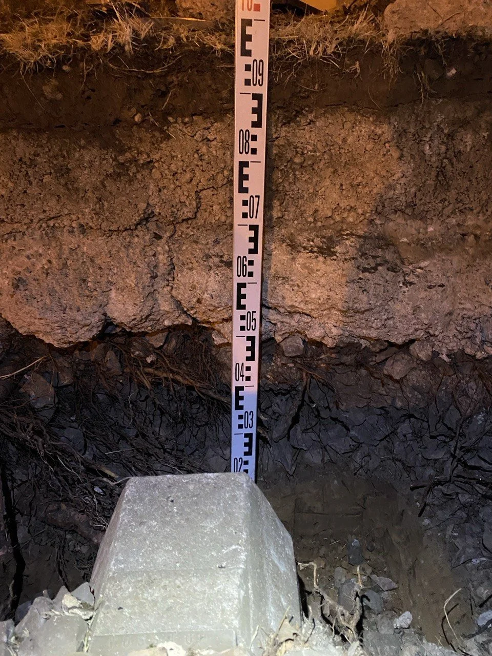 Ein Tiefbau-Messstab, der in einer Erdsohle steckt, zeigt die Position des Fußes eines Pfeilers, der etwa 1,28 Meter in die Erde reicht.