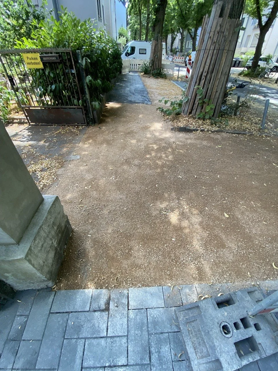 Fußweg in einer Stadt, mit Baustellenelementen, Bäumen und Fahrrädern im Hintergrund.