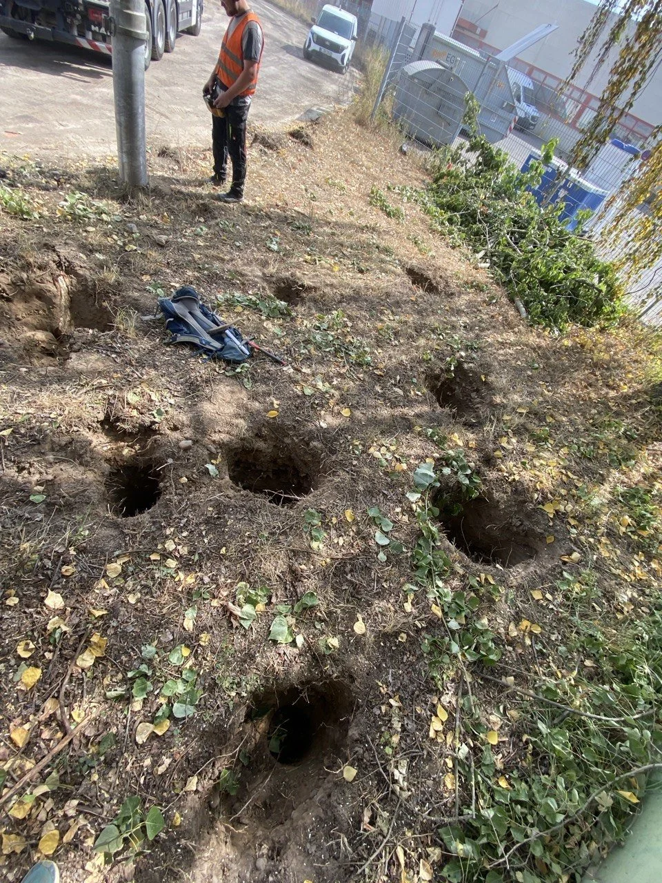 Bauarbeiter vor einem Zaun mit mehreren erstellten Erdgruben im Boden.