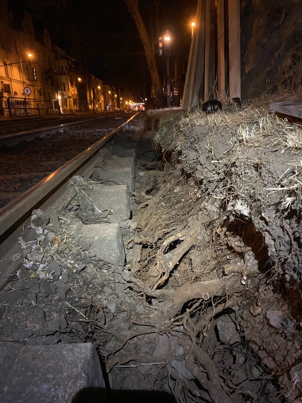 Ein Eisenbahngleis bei Nacht mit einer aufgerissenen Erdschicht auf einer Seite, sichtbar sind Wurzeln und Steine. Es scheint eine Schadensstelle an der Bahnlinie zu sein.