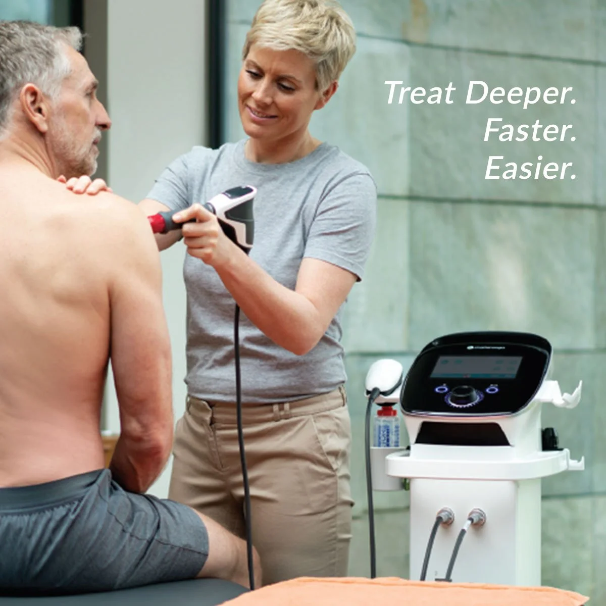 A woman performing shockwave therapy on a man in a clinical setting. The device is  connected to a machine with a digital display and controls.