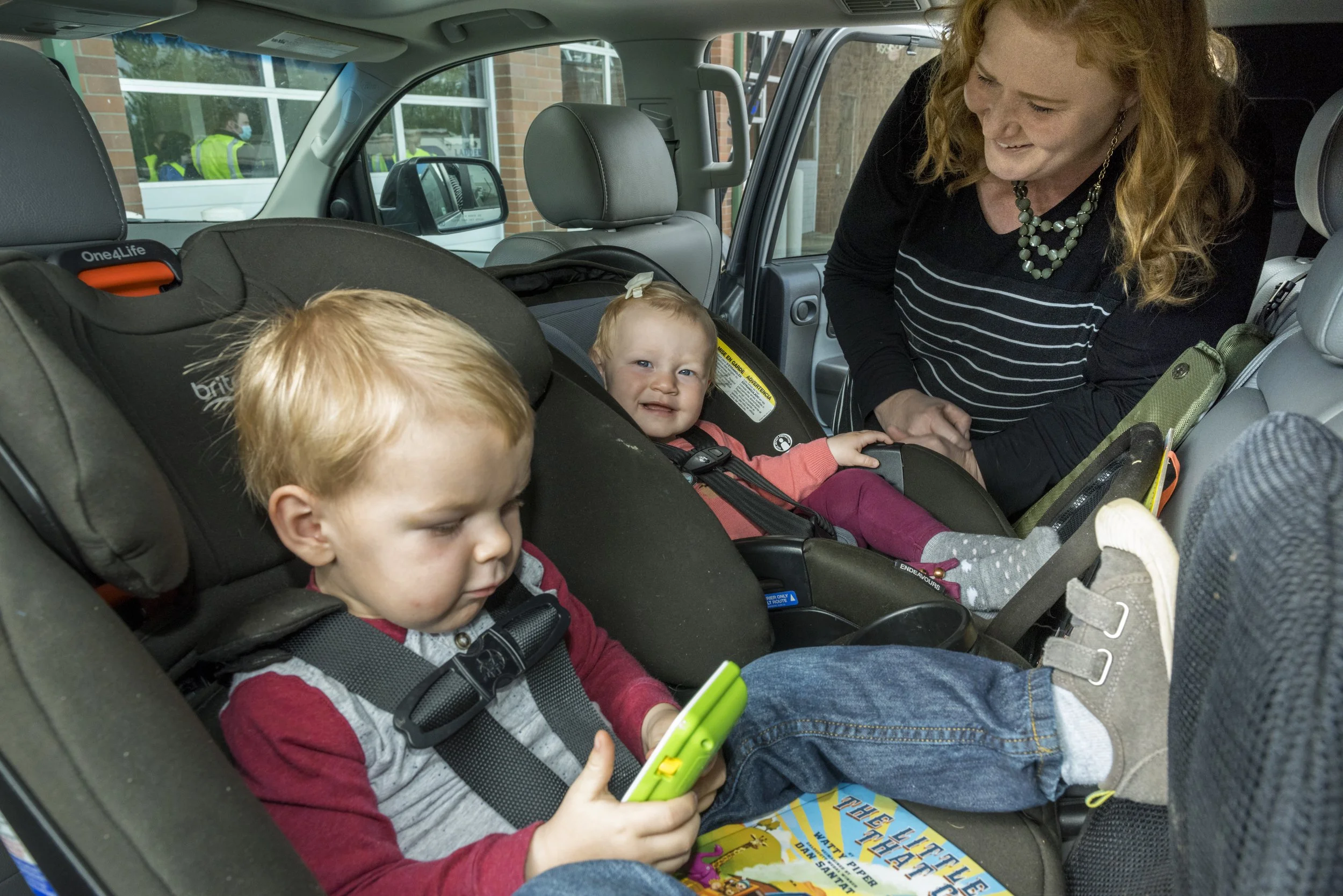 Image of adult woman smiling at two young children sitting in rear facing car seats in the back seat of a vehicle
