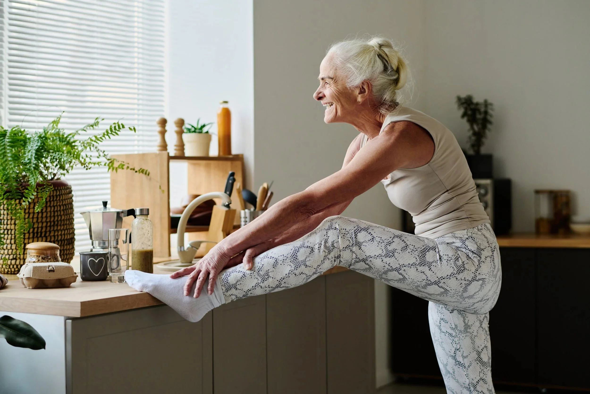 Older woman doing a leg stretch at her kitchen worktop