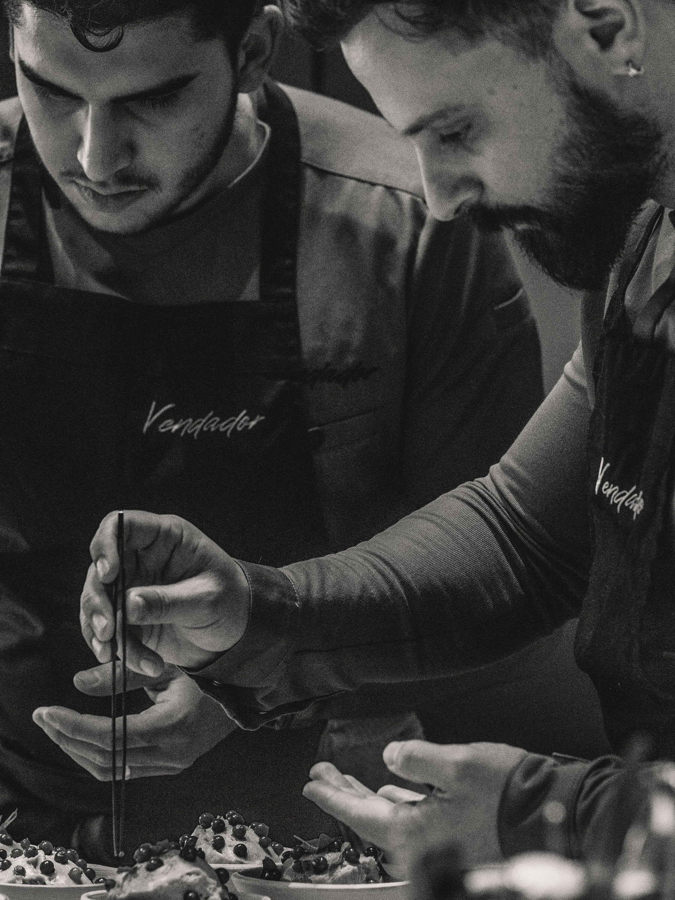 Two male bakers with aprons labeled 'Vendedor' decorating cakes with blueberries.