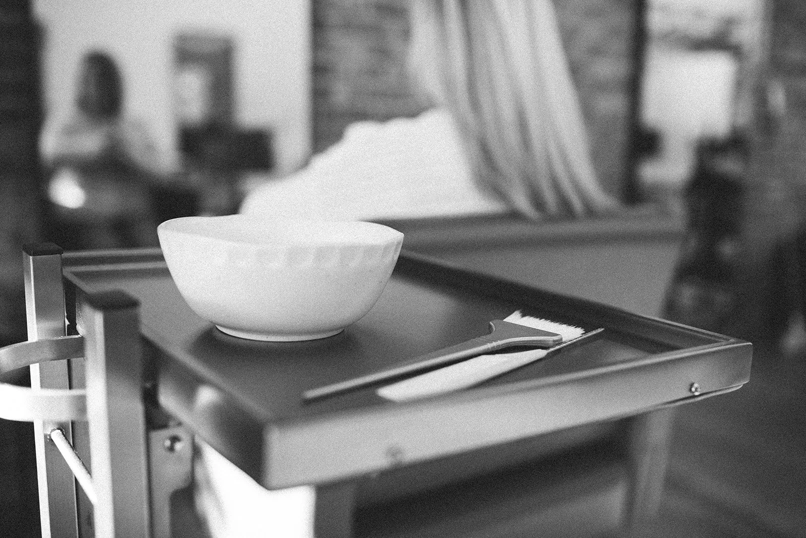 A small table with a white bowl and hair styling colorist tools In the background, a person is visible.