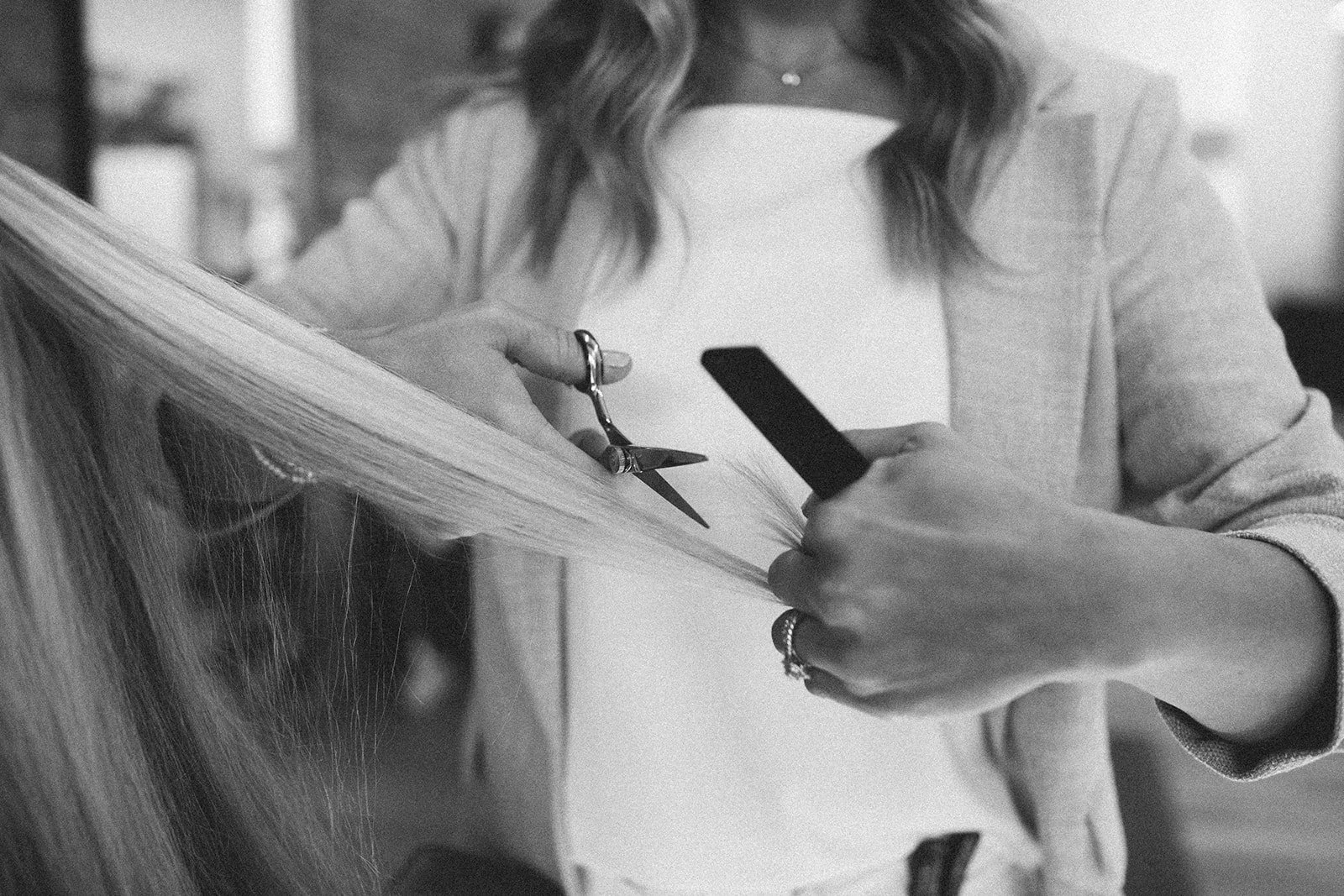 A person holding a pair of hair scissors and a comb, trimming long blonde hair.