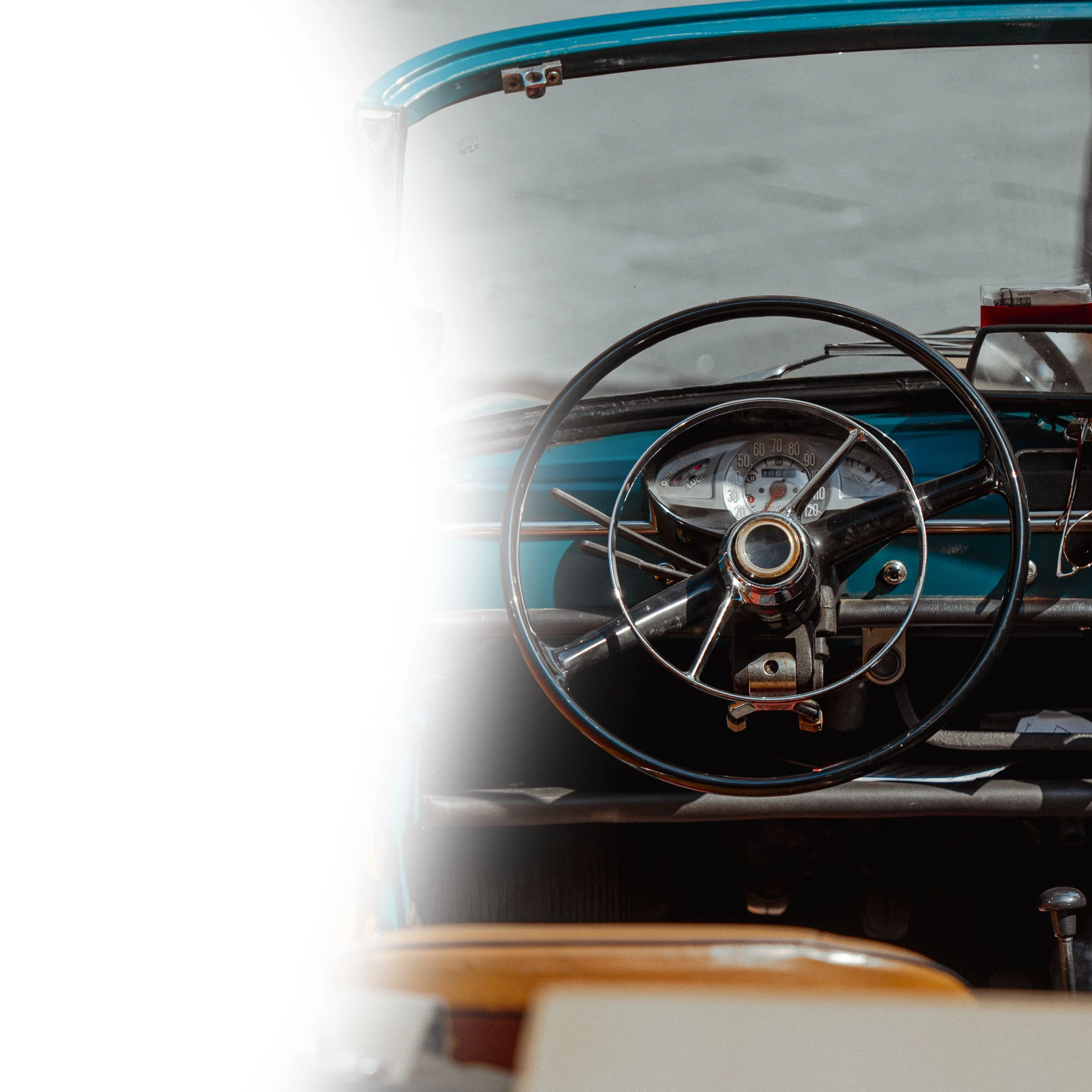 Close-up of a vintage car dashboard with a speedometer and steering wheel, with some sunlight shining onto the windshield.