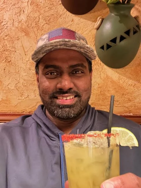 A person in a cap holding a cocktail with a lime wedge.