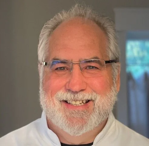 Smiling person with glasses and a beard wearing a white shirt