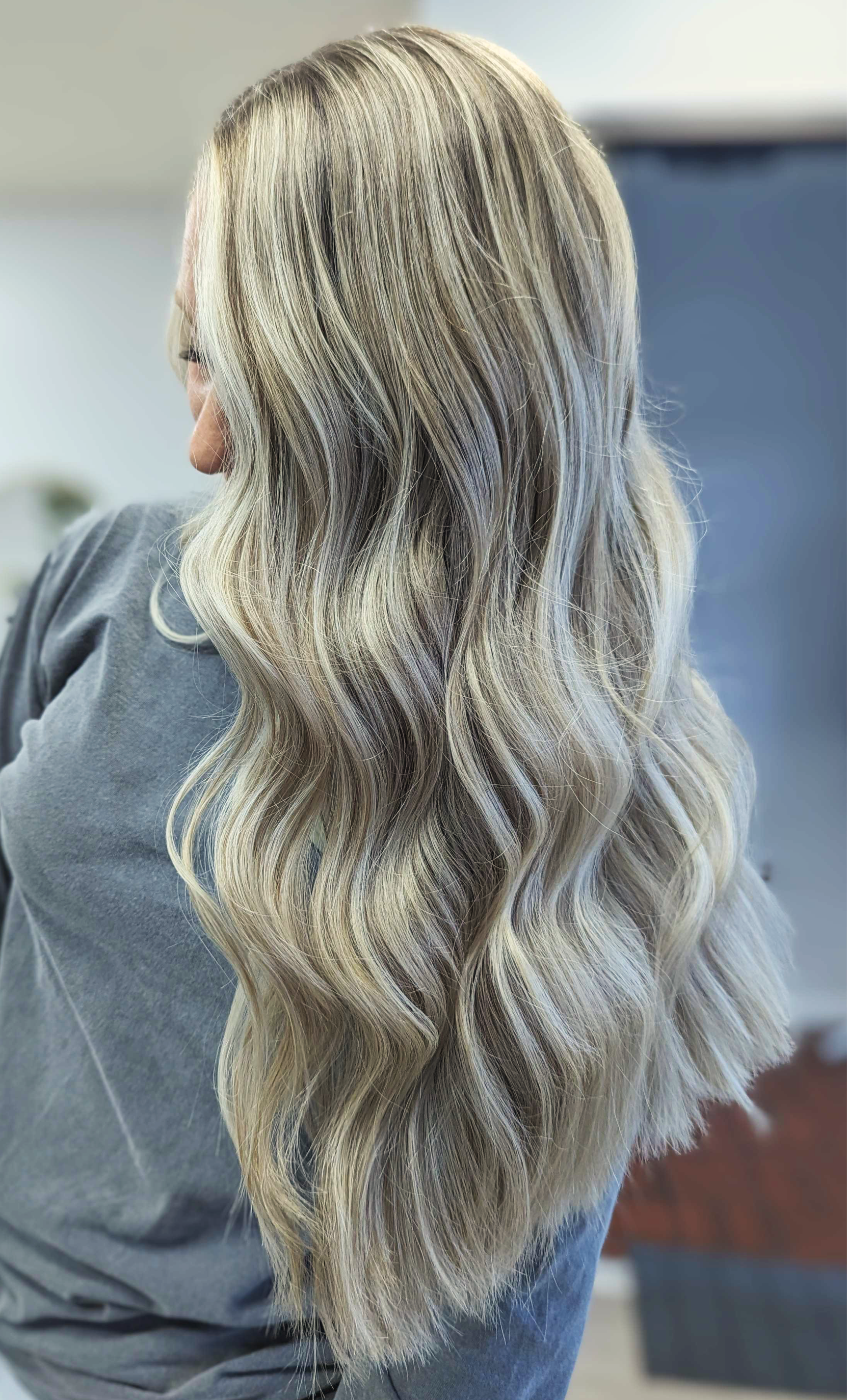 Woman with long, wavy blonde hair with darker roots, seen from behind.