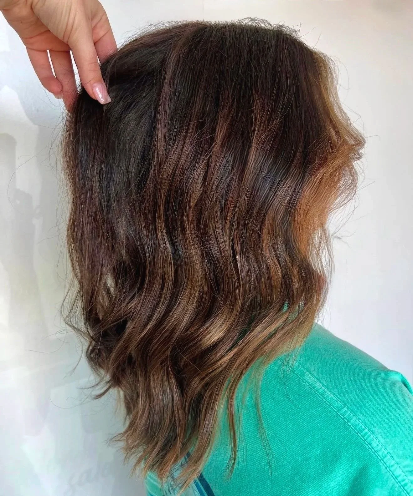 Side view of a woman with shoulder-length wavy hair, showcasing a blend of brunette and auburn hair colors.