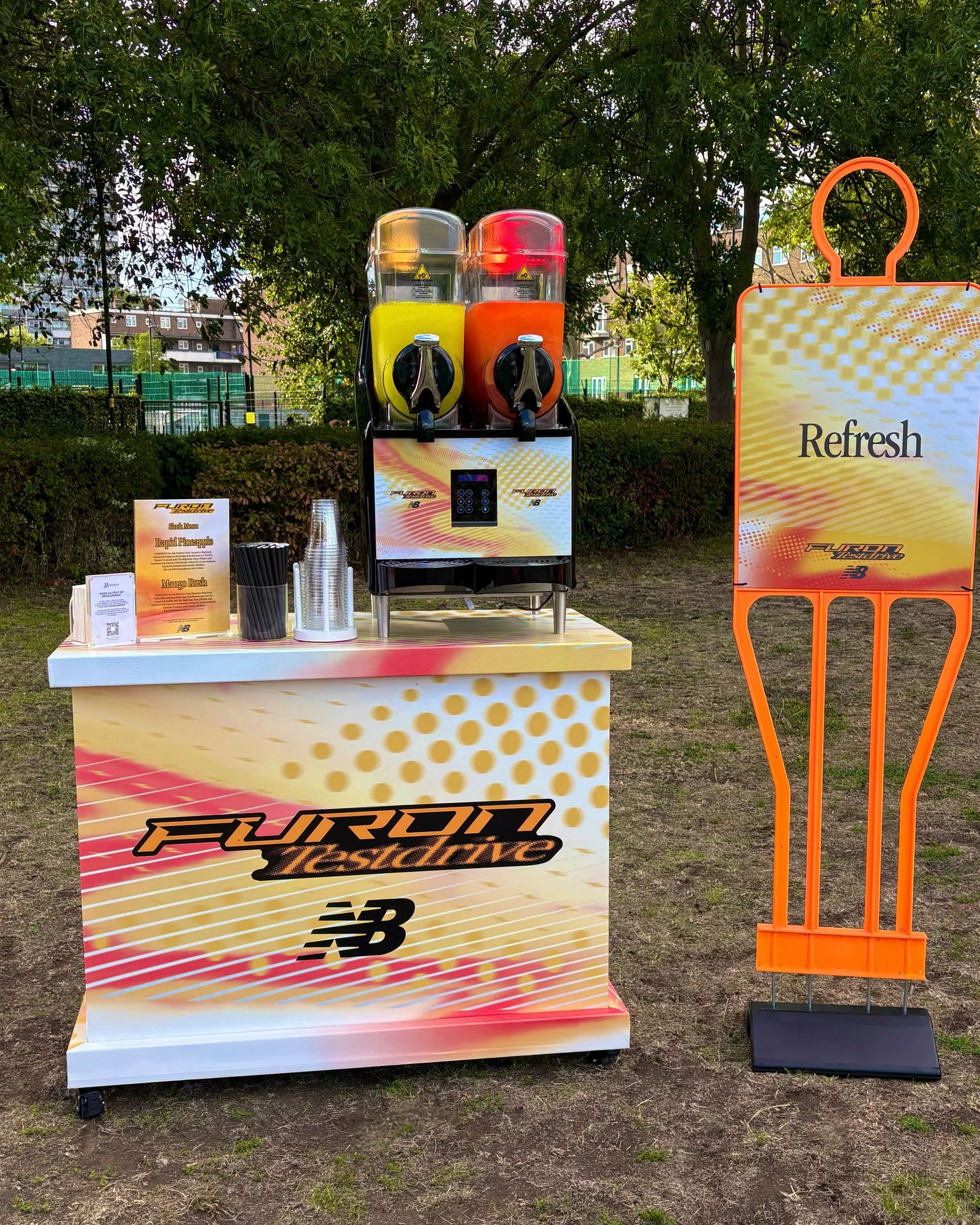 Custom branded New Balance Furon Test Drive slush cart with two slush machines serving Rapid Pineapple and Mango Rush, set up outdoors with an orange Refresh signage board beside it at a football activation in London.