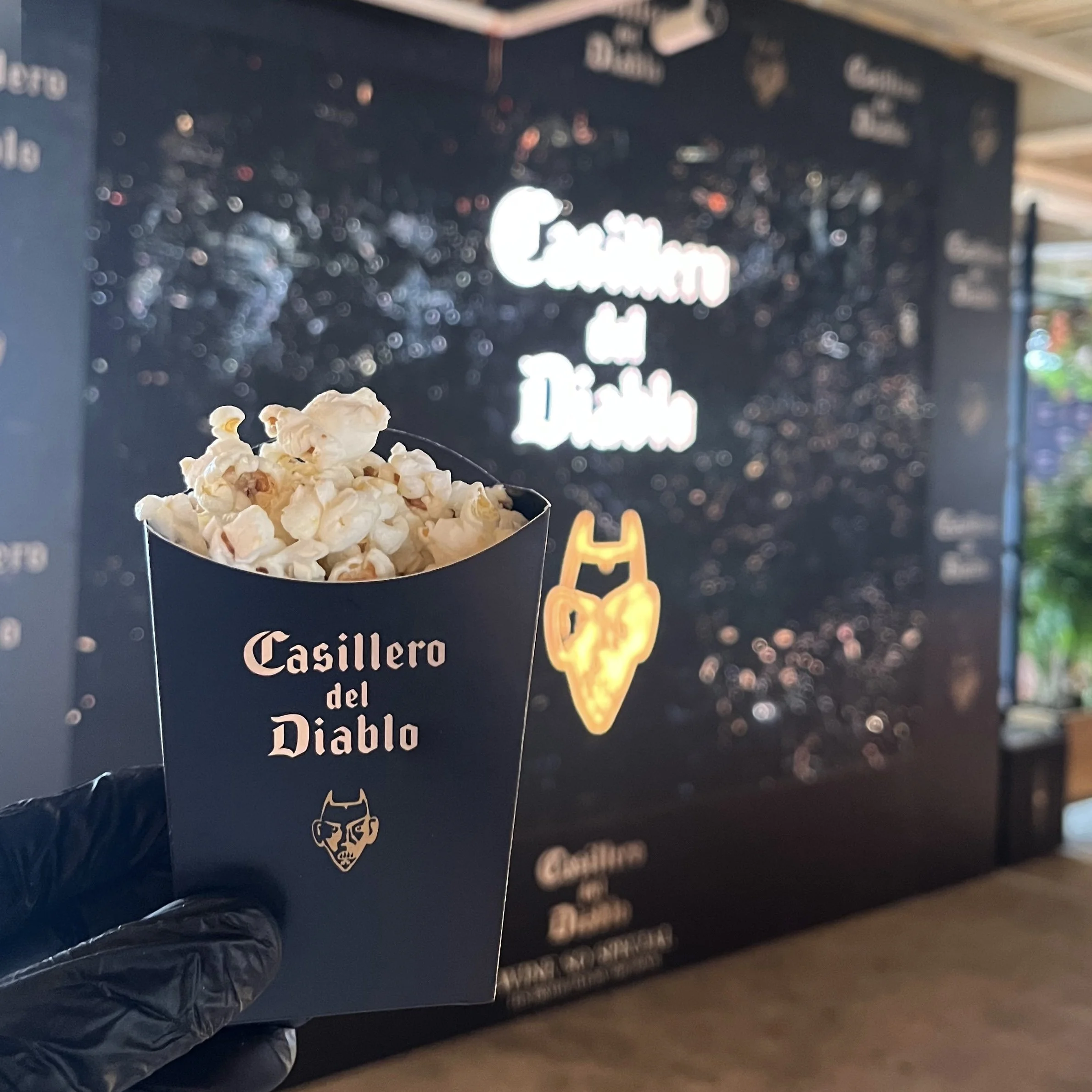 Guests gather around a popcorn cart with a digital screen, enjoying popcorn at a festive event.