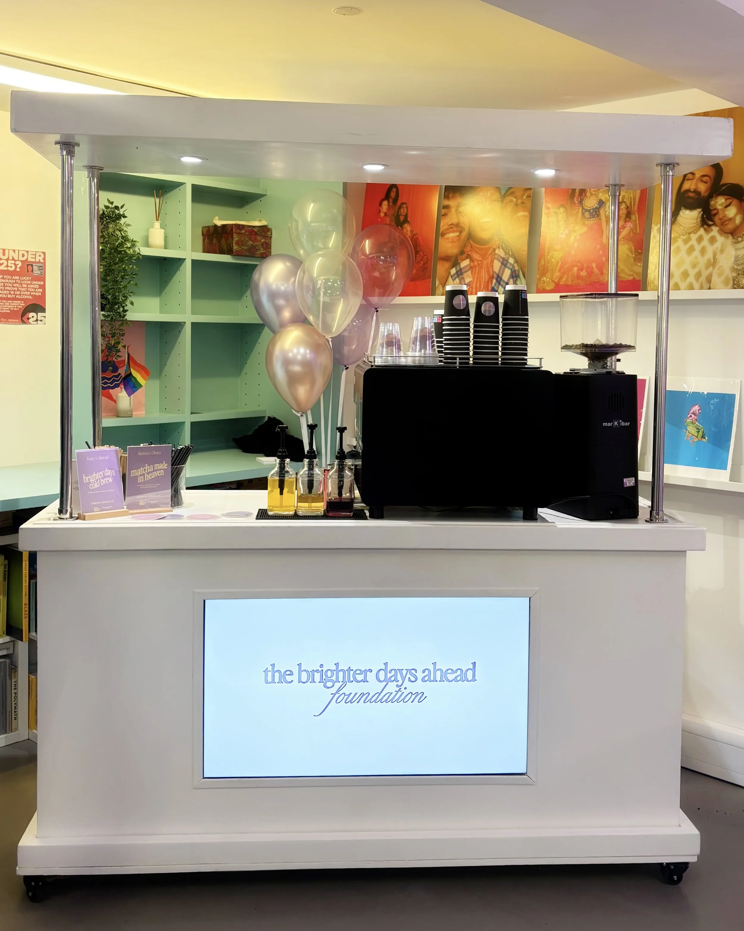 White coffee cart with a branded screen for The Brighter Days Ahead Foundation, decorated with balloons