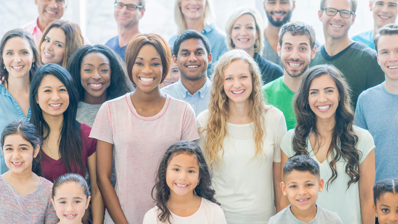 A diverse group of smiling adults and children posing together for a photo indoors.