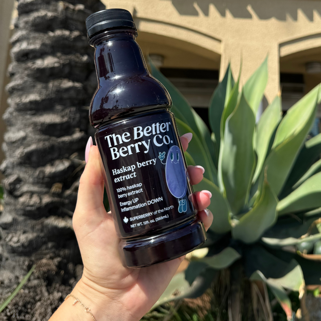 Hand holding a bottle of The Better Berry Co. haskap berry extract outdoors, with green plants in the background.