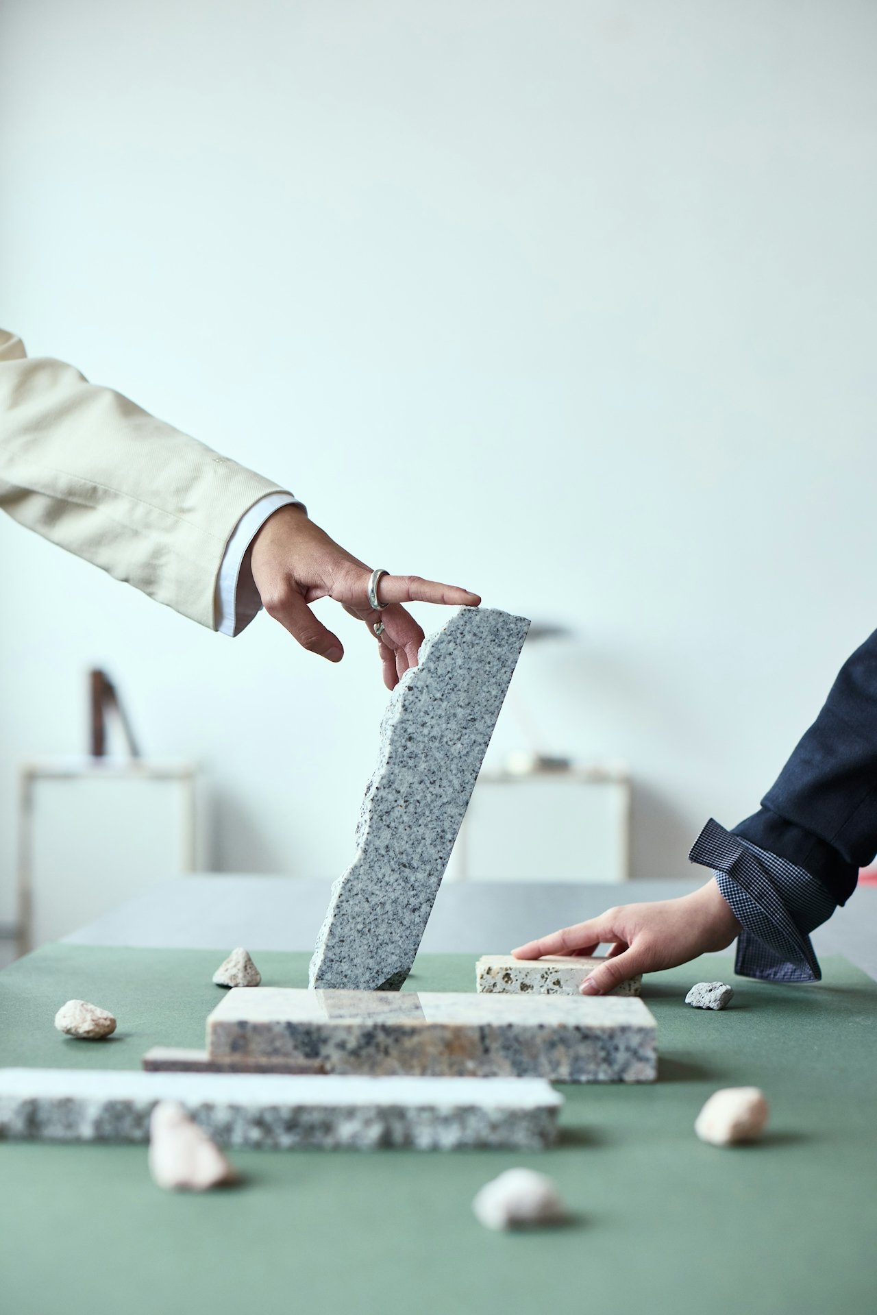Two individuals are stacking gray granite slabs on a green surface, with various small rocks around them.