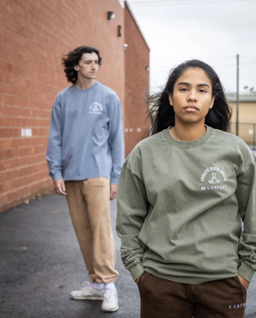 Two models wearing casual branded long-sleeve shirts walk outdoors along a brick wall, photographed with one model in the foreground and another behind.