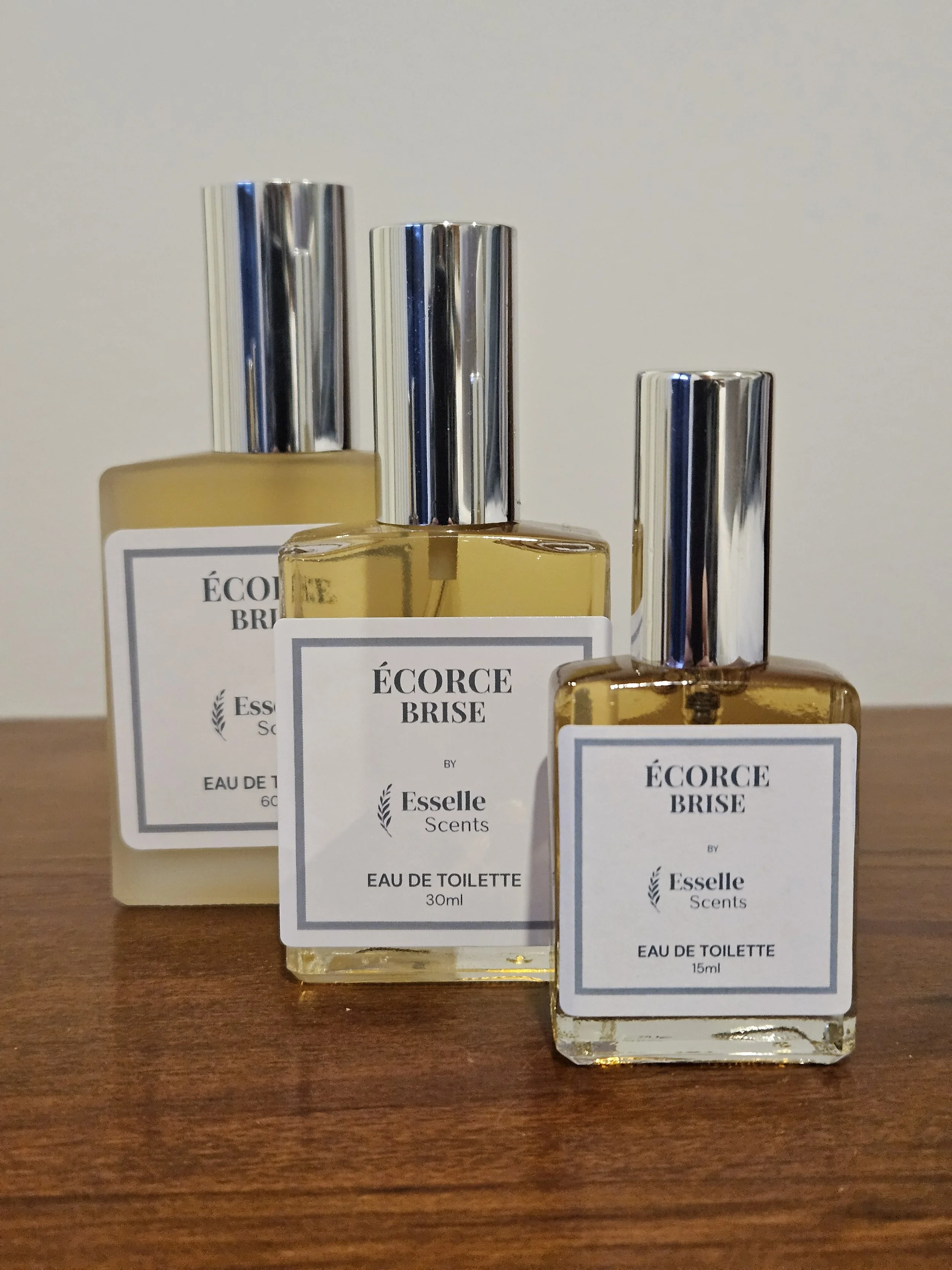 Three bottles of perfume labeled ÉCORCE BRISE by Esselle Scents placed on a wooden surface.