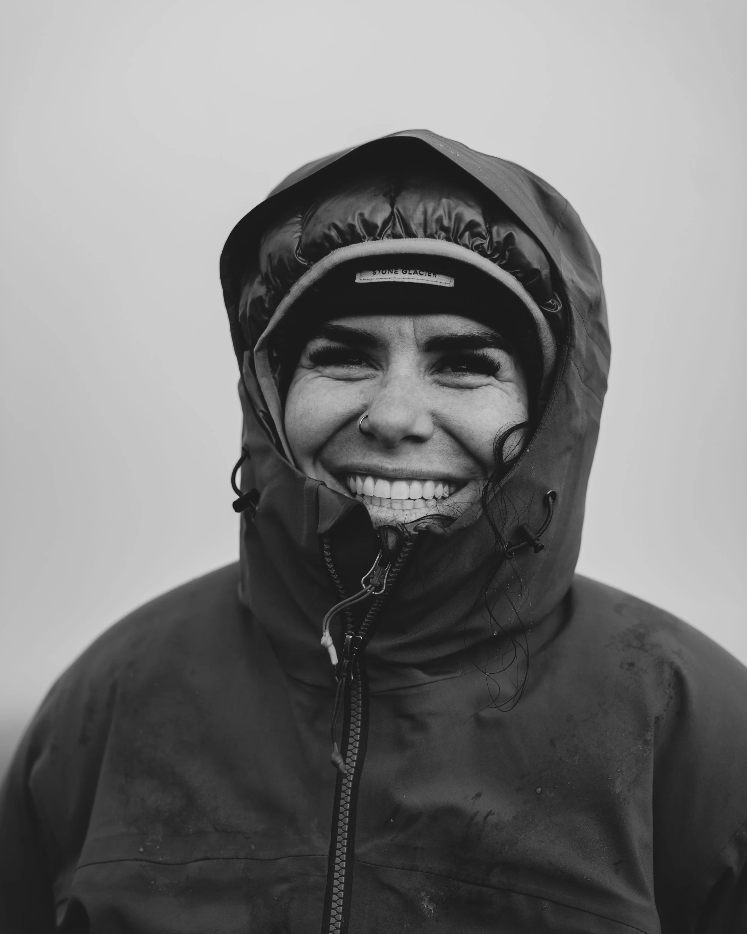 Melanie kirley Flow state productions marketing manager wearing a hooded jacket and a cap, smiling with eyes closed, in black and white.