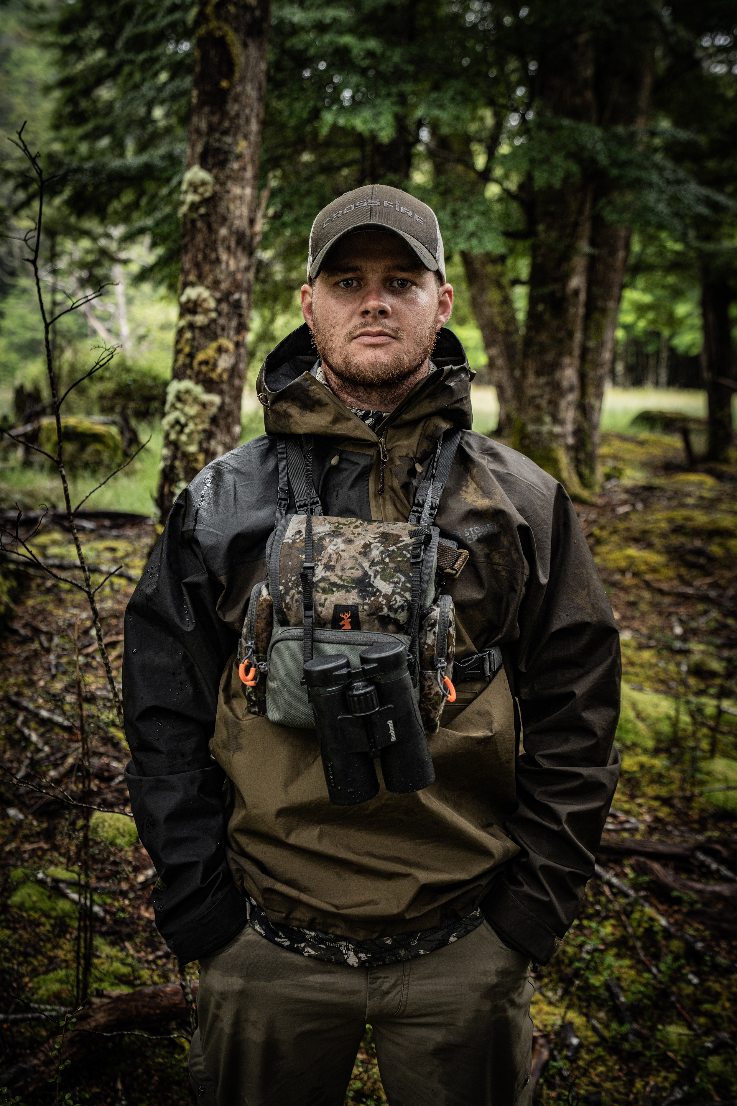 Man in outdoor camouflage gear and a cap standing in a wooded forest with trees and mossy ground. Flow State Productions Outdoor hinting Photography & videography