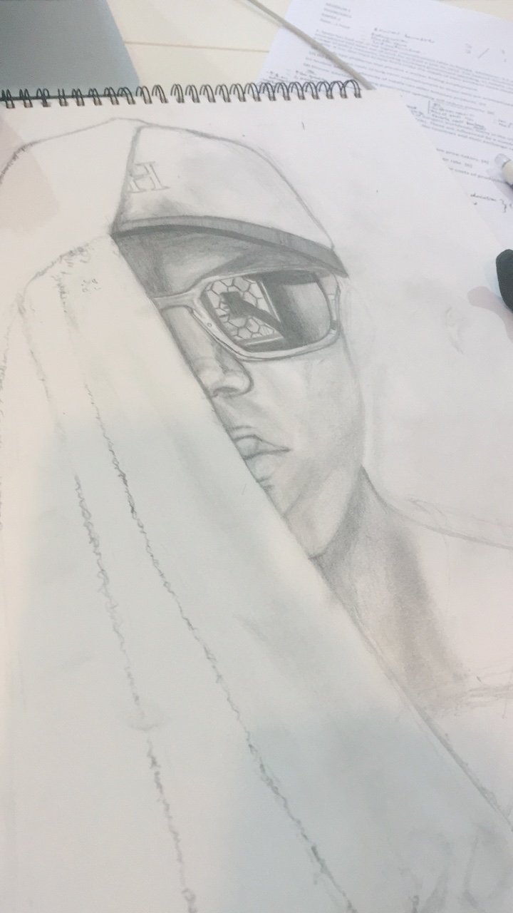 Pencil sketch of a woman wearing glasses and a cap, partially covered by a piece of paper, on a desk with scattered papers and a pen.