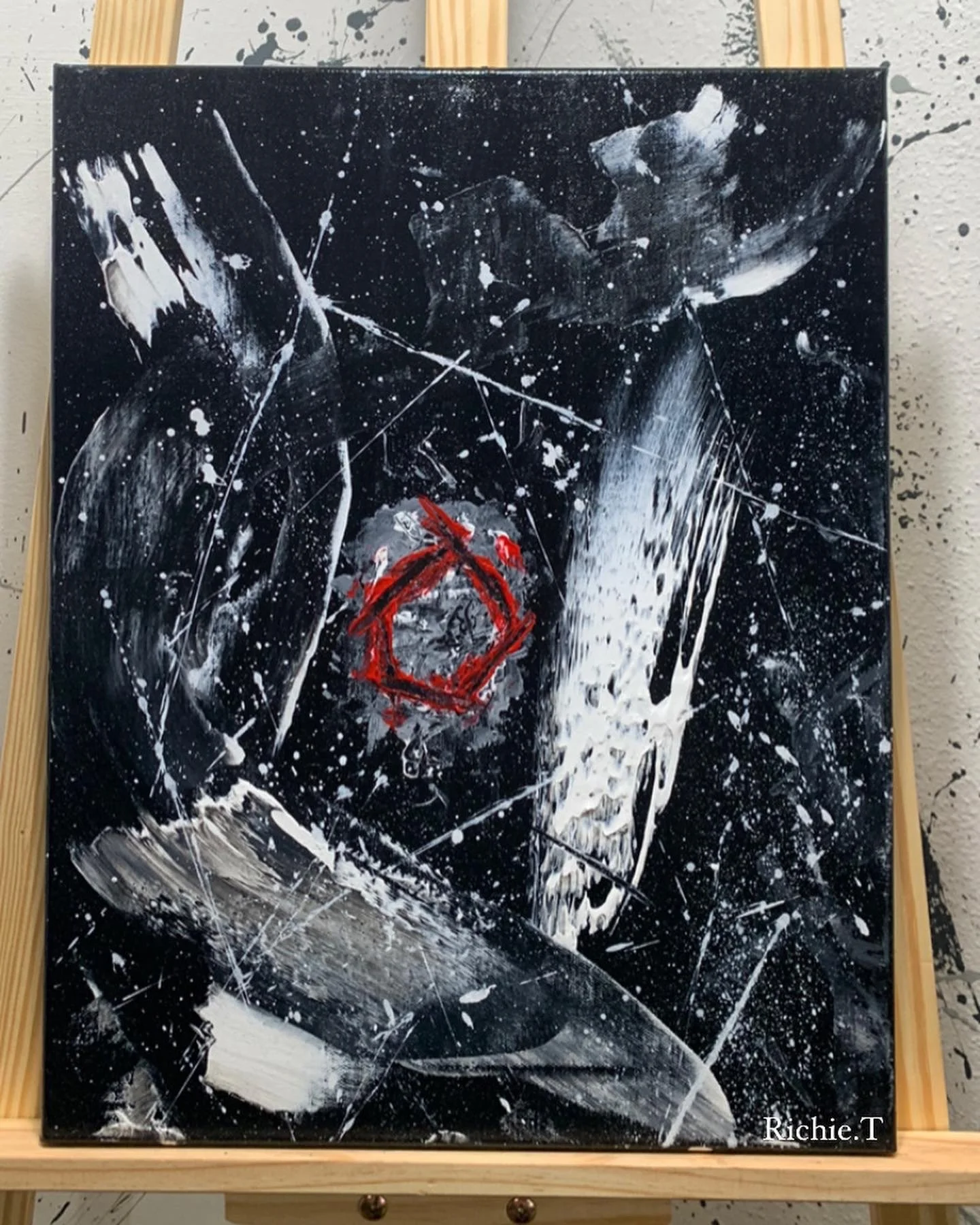 Abstract painting with black background, white splatters, strokes, and lines, featuring a red geometric shape at the center, signed 'Richie T' at the bottom right corner.