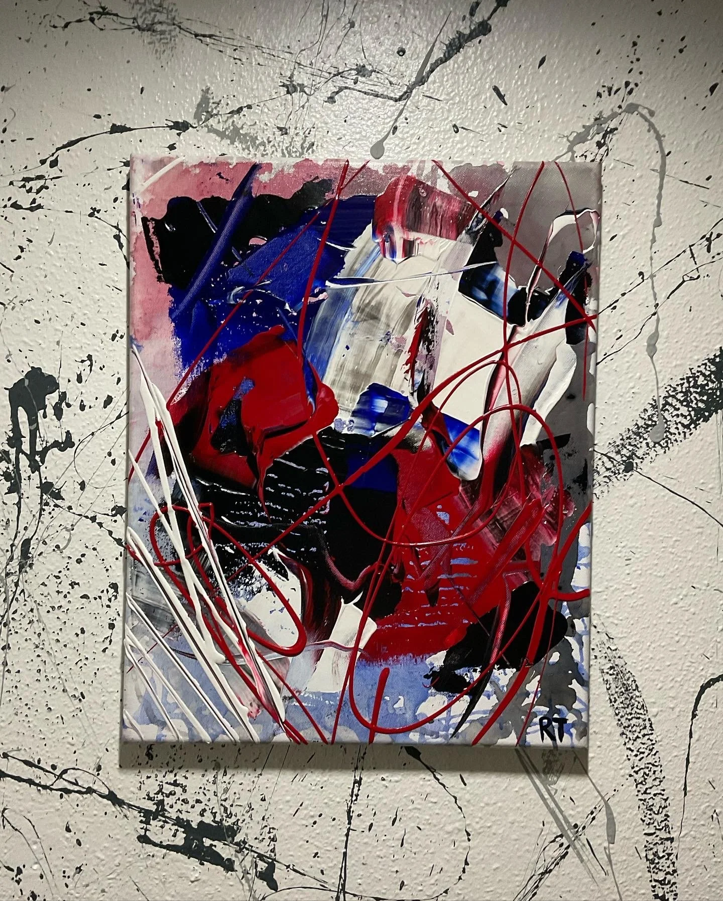 Abstract painting with red, blue, black, white, and gray paint on a canvas, with red string and black and gray splatter on white textured background.