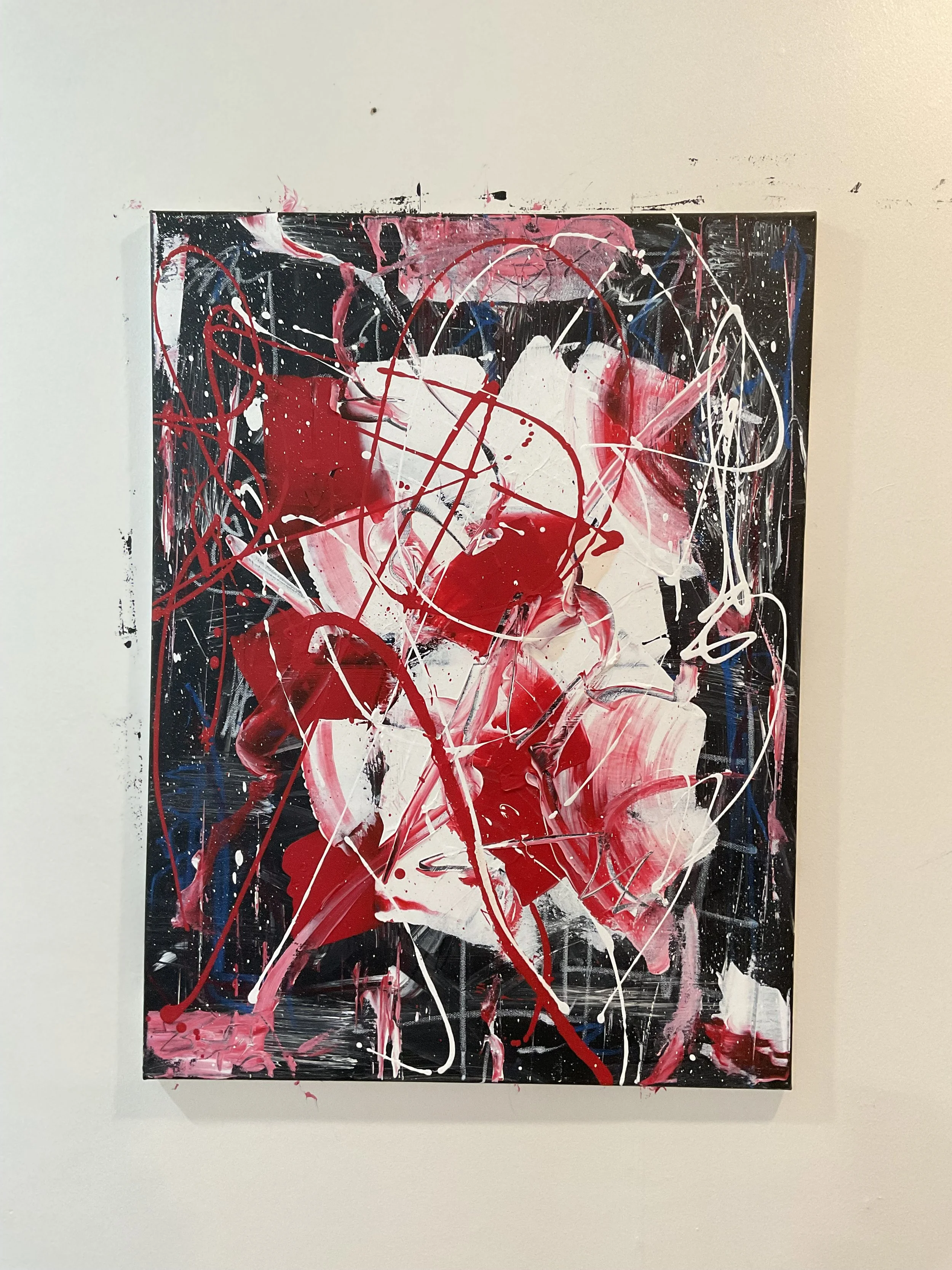 Abstract expressionist painting with black, white, red, pink, and blue paint splatters and drips on canvas.