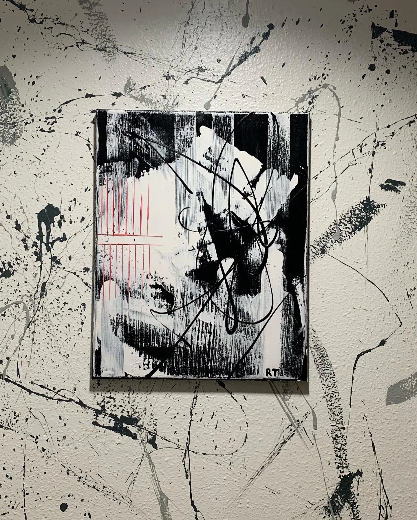 A black and white portrait of a woman with short hair, painted in a graffiti style, signed with initials 'RT' in the bottom right corner, on a splattered abstract background.