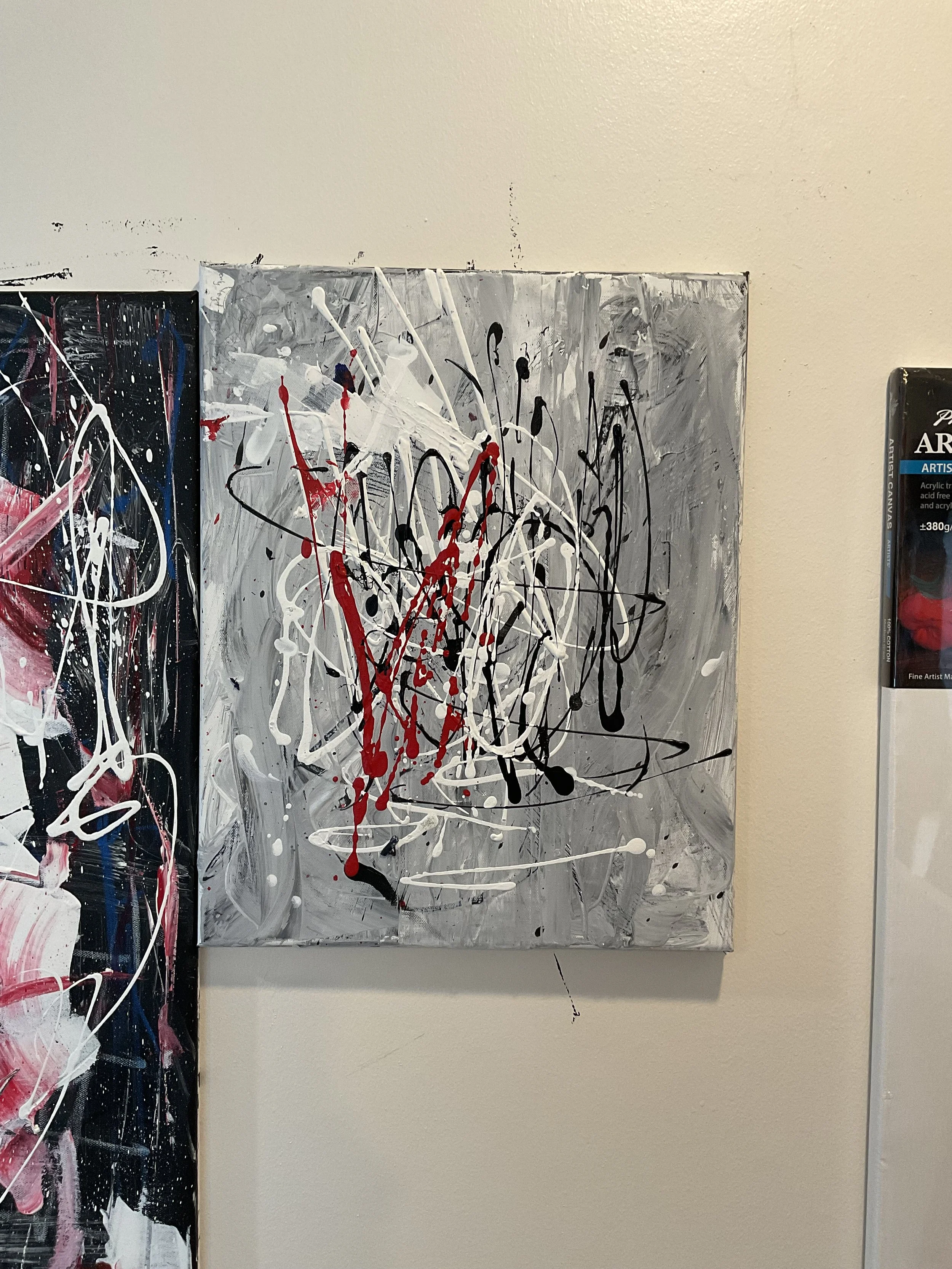 Abstract painting with splashes of black, white, red, and gray paint on a gray background.