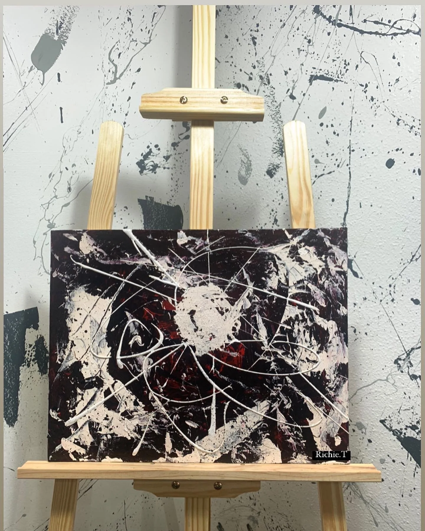 Abstract expressionist painting on a canvas with black, white, and red splatters and swirl patterns, signed by Richie T.
