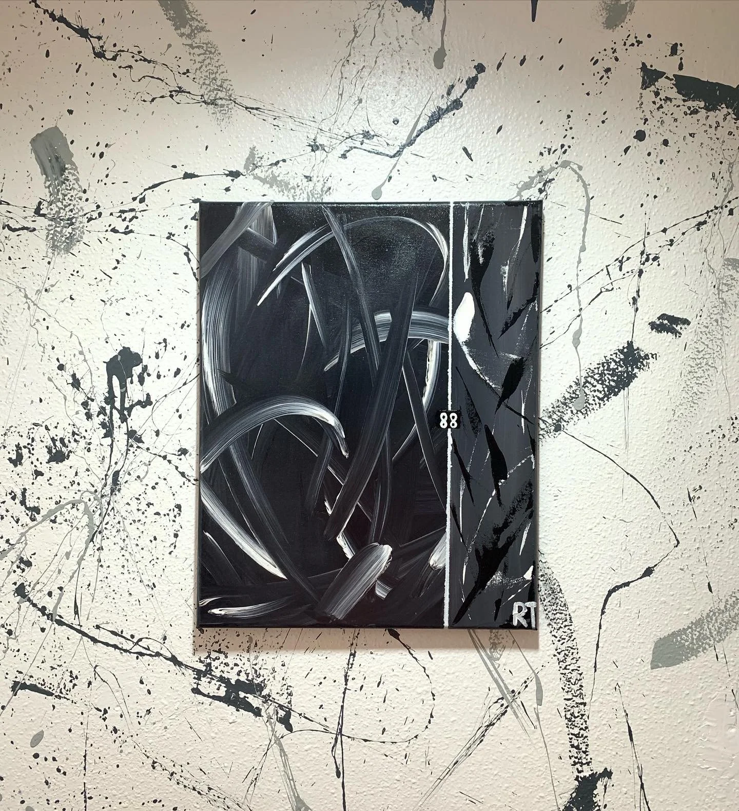 Abstract black and white painting with bold strokes, small numbers '88' and the initials 'RT' on a splattered wall.