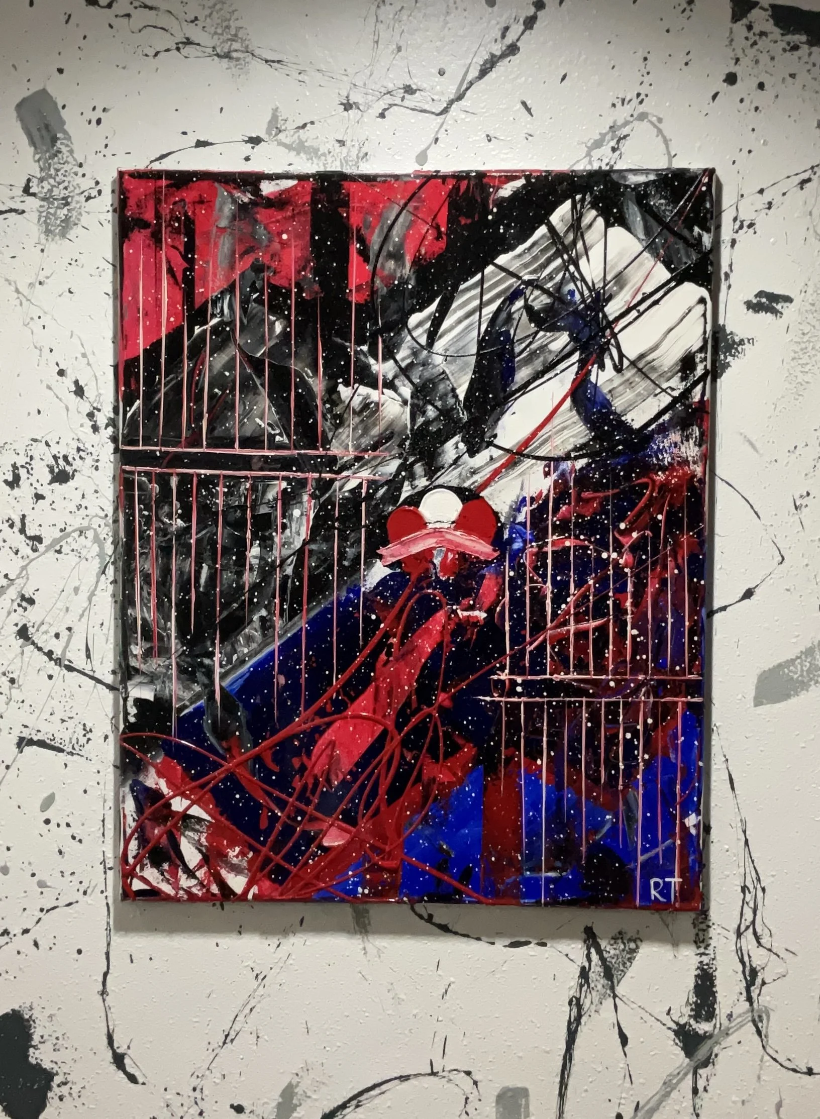 Abstract artwork with black, red, white, and blue paint splatters and drips on a canvas, featuring a central red and white clown face.