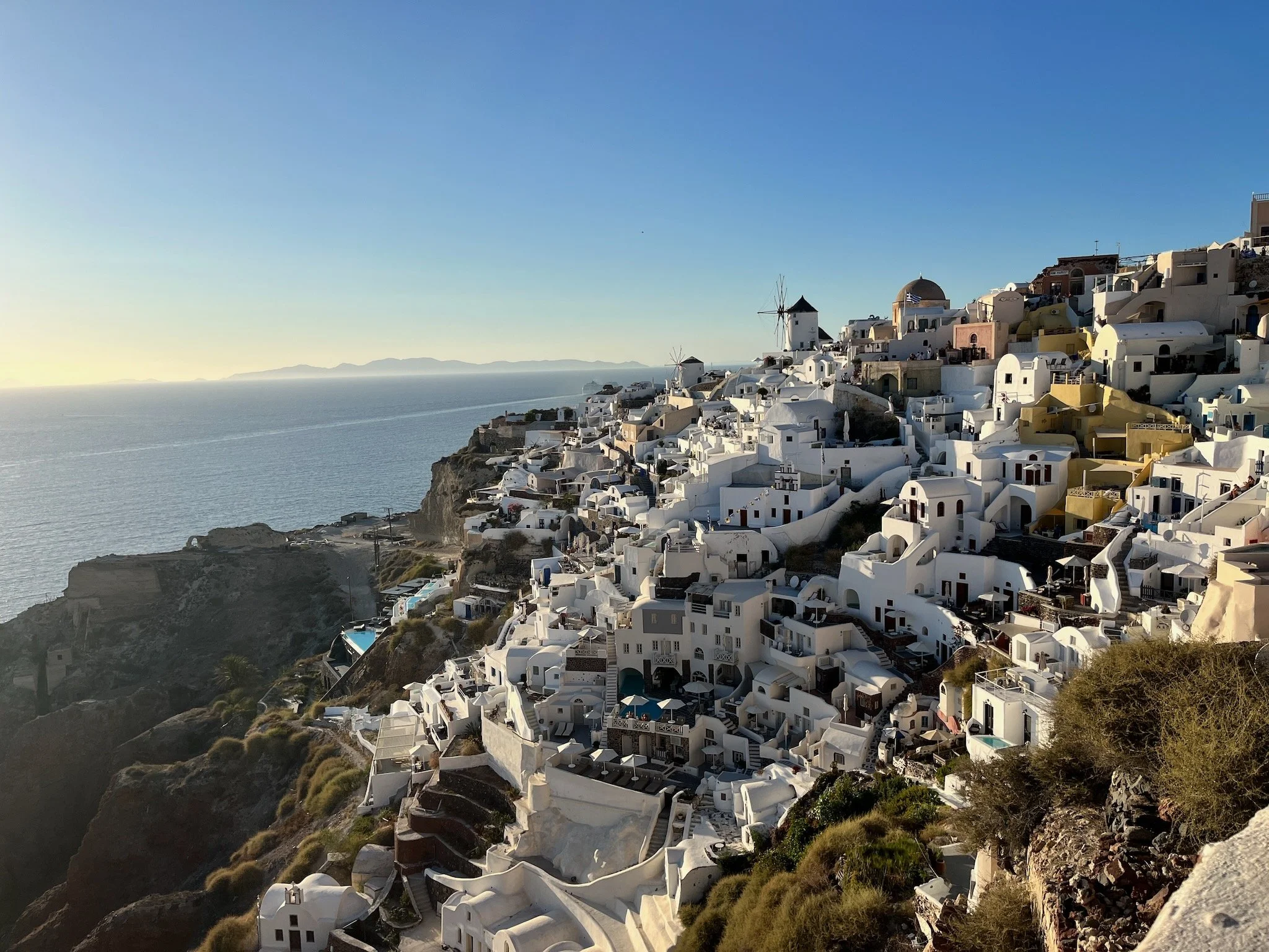 White hillside buildings overlooking the caldera of Santorini in the Cyclades, in Greece, with windmill on a cliff overlooking the sea at sunset in Santorini, Greece.