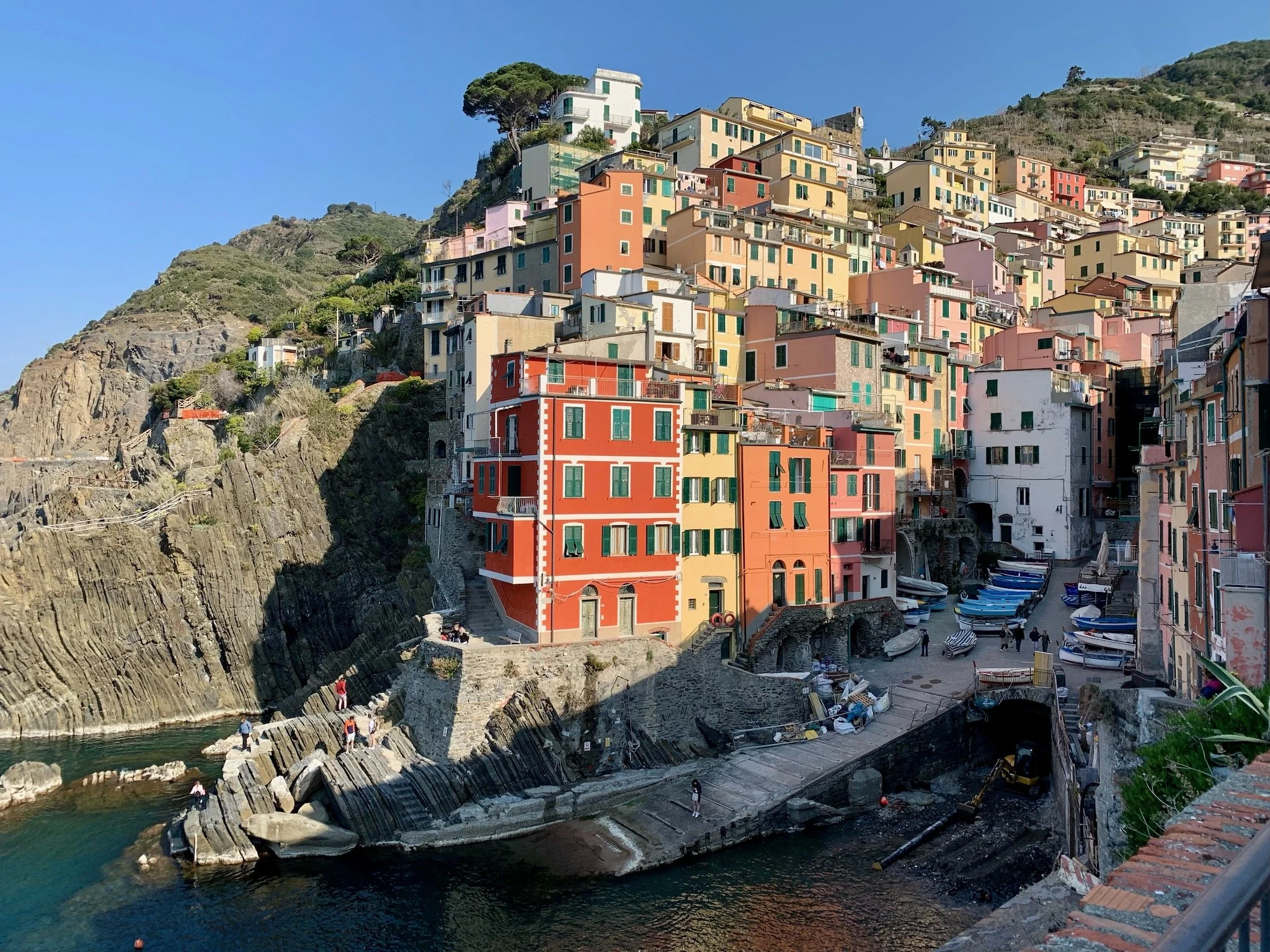 The colorful houses of Riomaggiore, in Cinque Terre, Italy, built on a hillside overlooking the water in a coastal village, with boats docked near the shore.
