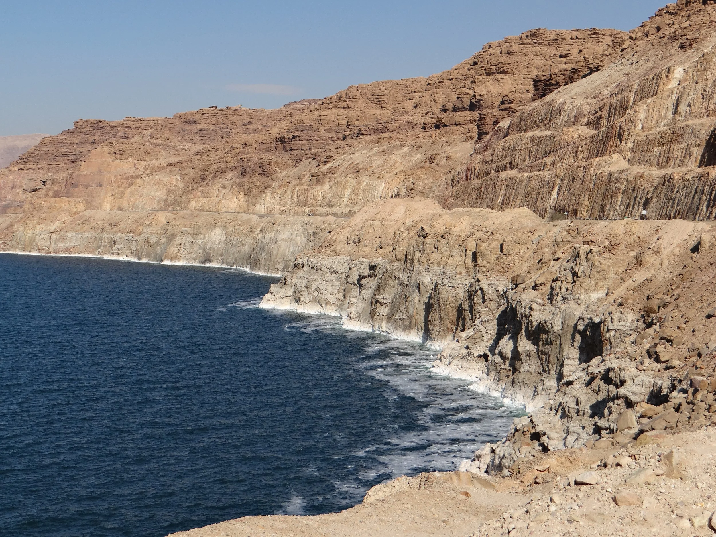 Cliffs along the shoreline of the Dead Sea, in Jordan, with visible layers of sedimentary rock and waves crashing against the rocks.