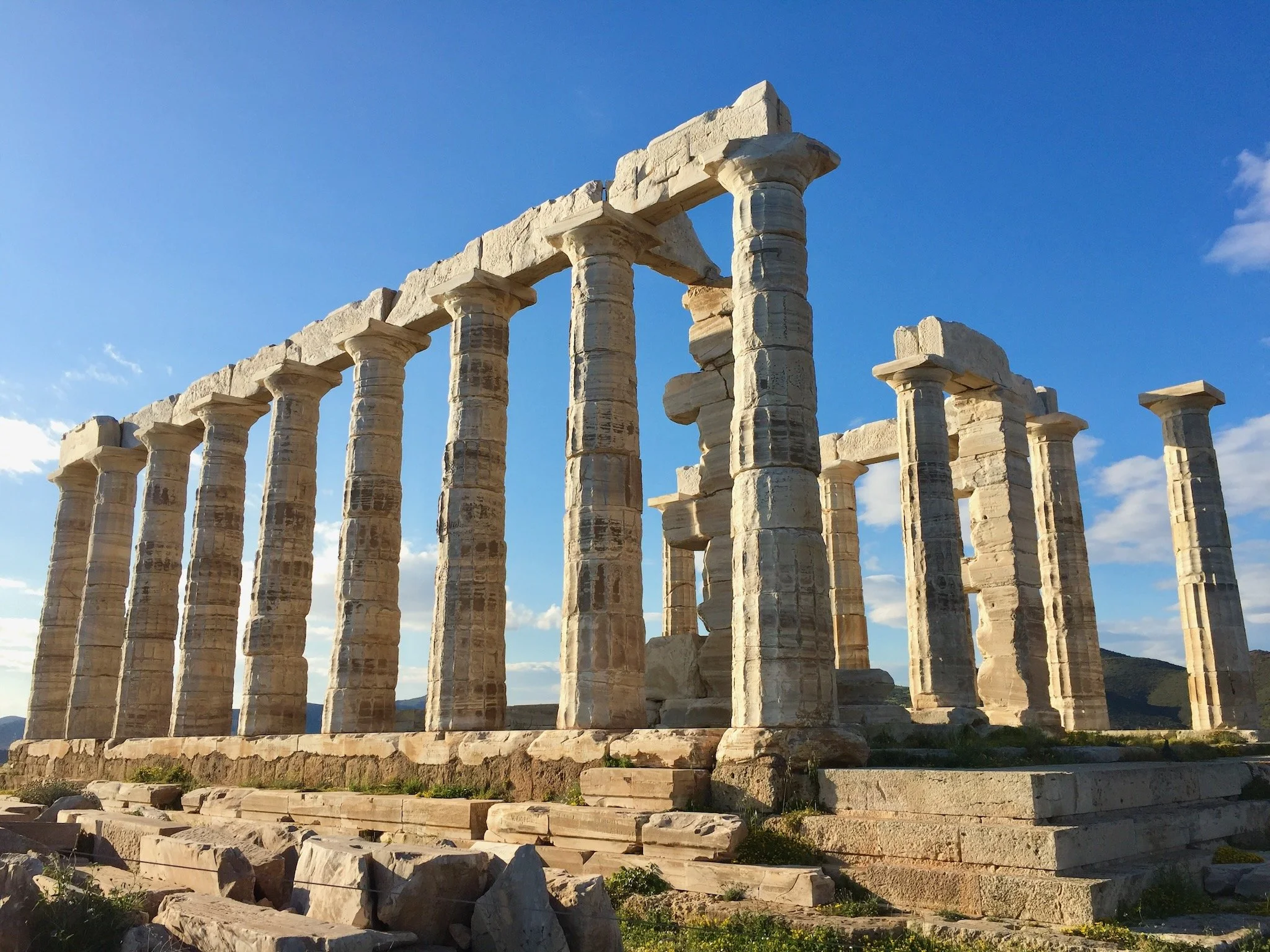 Ancient Greek temple ruins at Cape Sounio, Greece with tall stone columns under a blue sky with clouds.