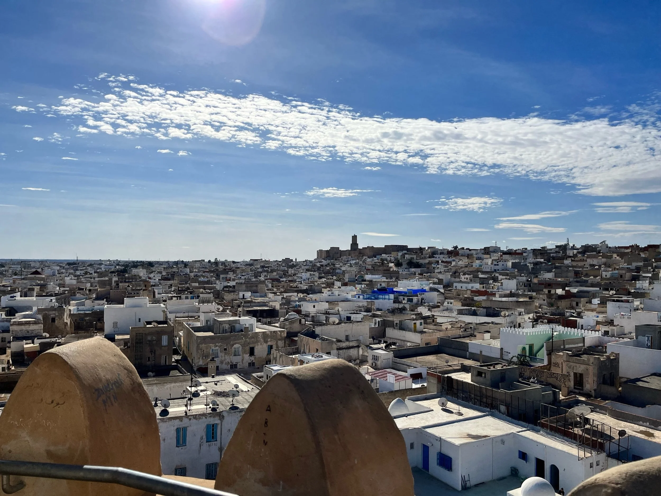 Scenic view of the medina in the city of Sousse, Tunisia, with white buildings under a clear blue sky with scattered clouds, taken from a high vantage point.