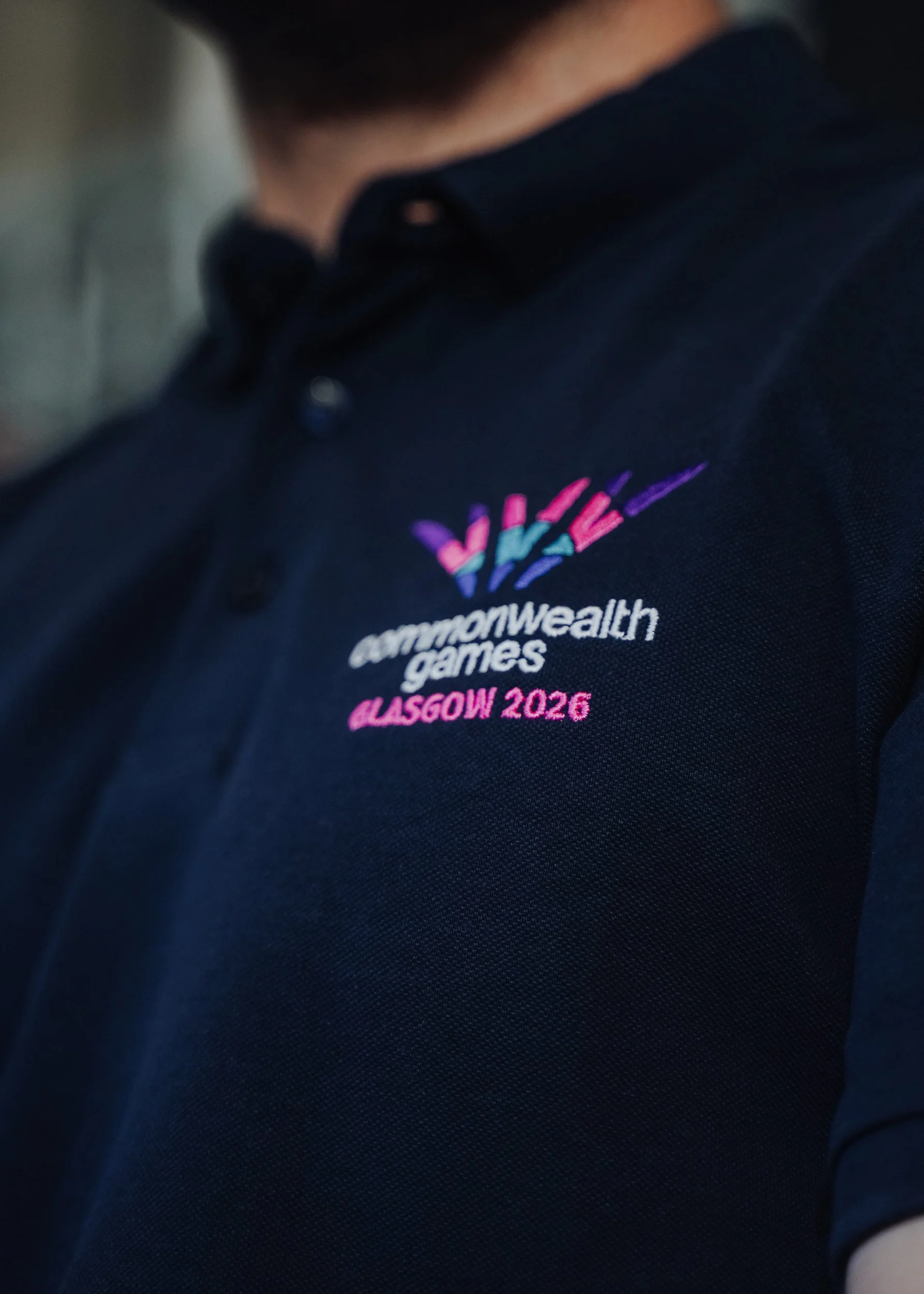 Close-up of a navy blue polo shirt with an embroidered logo for the Commonwealth Games in Glasgow 2026.