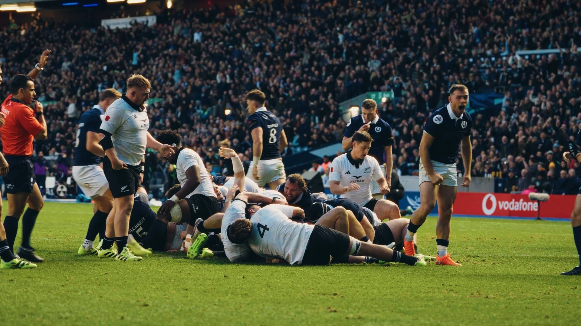 Rugby players celebrating a try on the field during a match, with a large crowd of spectators in the background.