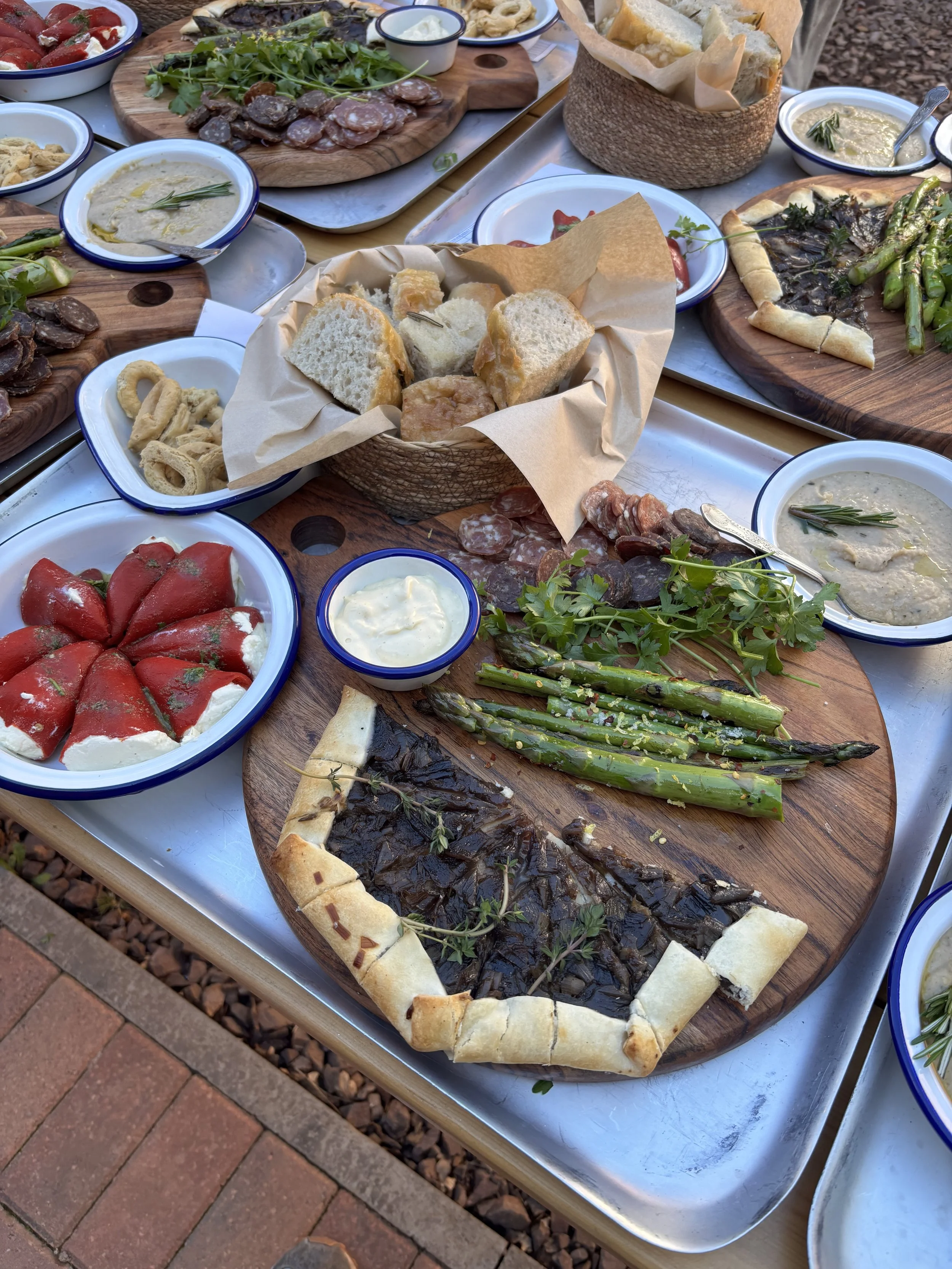 A spread of assorted dishes including roasted vegetables, bread, dips, and salads on a metal tray and wooden serving boards.