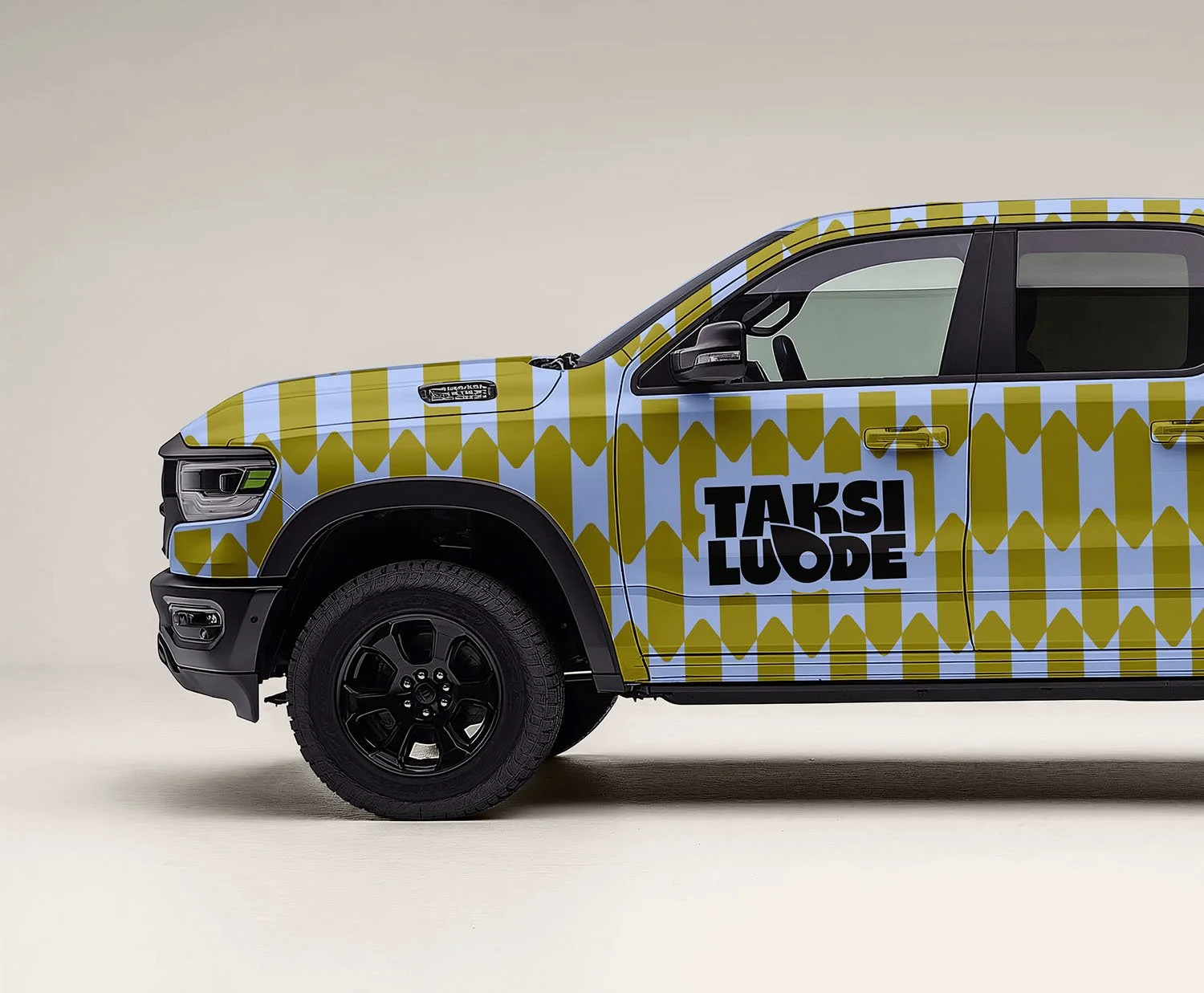 Valkoisella taustalla oli auton kyljessä suuret mustat kirjaimet lukevat "TAKSI LUODE" ja auto on päällystetty suomen lipun väreillä ja kuvioilla.